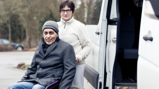 caregiver helping senior man with van at their back