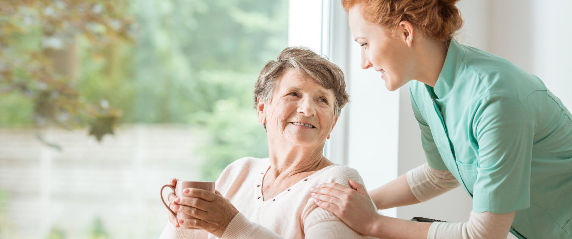 senior woman holding glass and female caregiver looking at each other