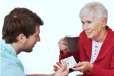 senior woman holding glass and medicines while caregiver assisting her